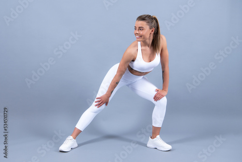 Sporty woman in sportswear doing stretching. Sports clothing, sportswear. Young beautiful model stretching out before training on gray studio background.