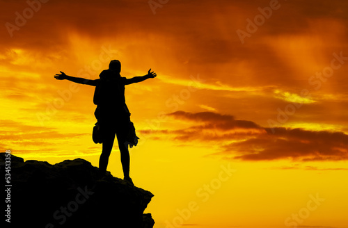 Dark silhouette, celebrate hiking and man with freedom while trekking in nature, success on adventure in sunset and travel on mountain of Canada. Person on cliff walking with joy on holiday in summer