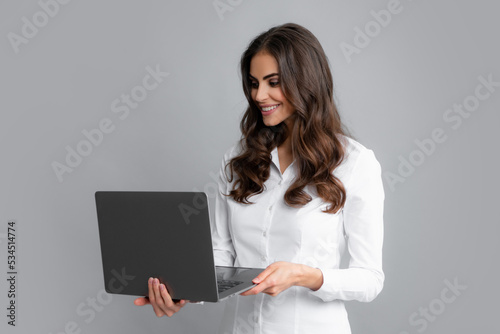 Beautiful smiling business woman over grey background using laptop computer.