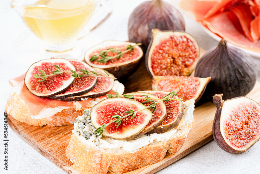 Bruschetta with raw ripe fig, blue and cream cheese, prosciutto, walnuts and herbs on wooden serving board. Healthy quick breakfast idea. Italian cuisine. Selective focus Bruschetta with raw ripe fig, blue and cream cheese, prosciutto, walnuts and herbs on wooden serving board. Healthy quick breakfast idea. Italian cuisine. Selective focus