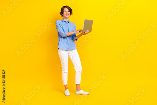 Full size photo of adorable gorgeous woman with bob hairstyle wear white pants setting tasks on laptop isolated on yellow color background