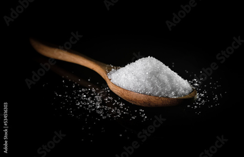 White sugar in wooden spoon on dark table background. Sweet seasoning.