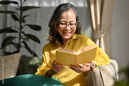 Фотография Senior woman sitting back on sofa with interesting book, Domestic life with senior people concept