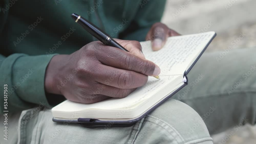 African young handsome man writing notes on his agenda on steps