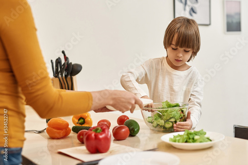 Boy taking salad for putting on plate for mother