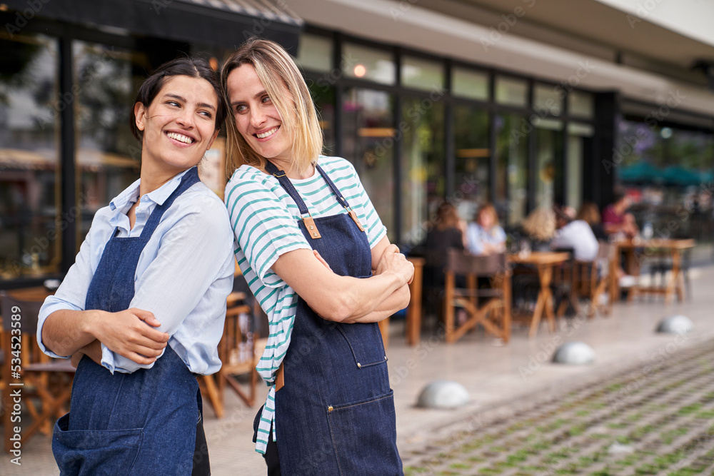 Portrait of two happy female restaurant business owners posing and having fun in front of their restaurant