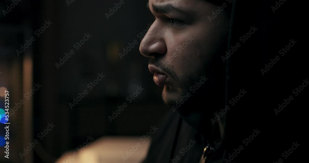 Close-up of bearded man looking intently at computer monitor and watching file data changes. The guy holds pen in hands and notes the main indicators. He is wearing black sweater and hat. Close-up of bearded man looking intently at computer monitor and watching file data changes. The guy holds pen in hands and notes the main indicators. He is wearing black sweater and hat.