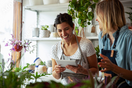 Cheerful flower shop female owners holding digital tablet
