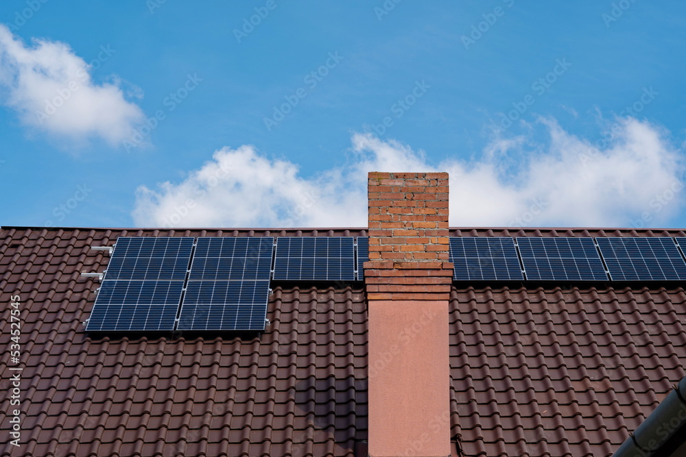 Solar panels mounted on the rooftop of a residential house. Sunny blue sky, brick chimney, no people Solar panels mounted on the rooftop of a residential house. Sunny blue sky, brick chimney, no people