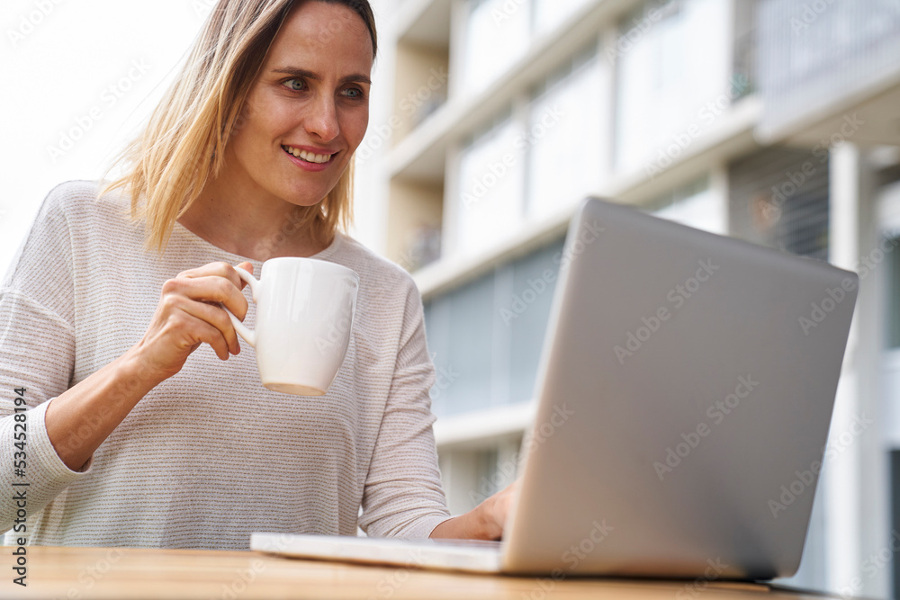 Low angle view of female entrpreneur looking at laptop screen and drinking coffee Low angle view of female entrpreneur looking at laptop screen and drinking coffee