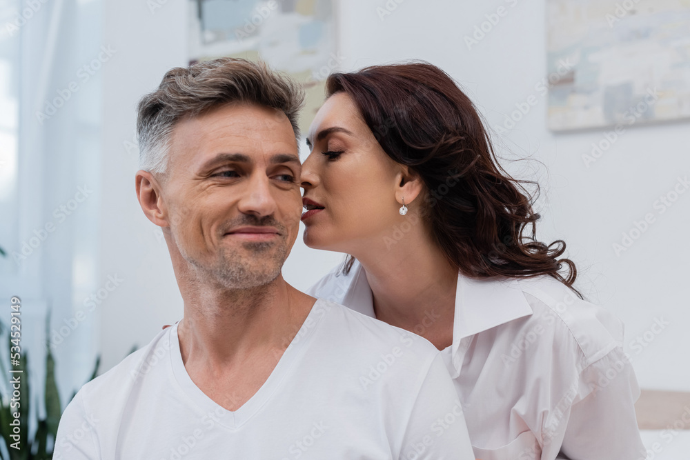 Brunette woman in shirt kissing smiling husband at home. Brunette woman in shirt kissing smiling husband at home.