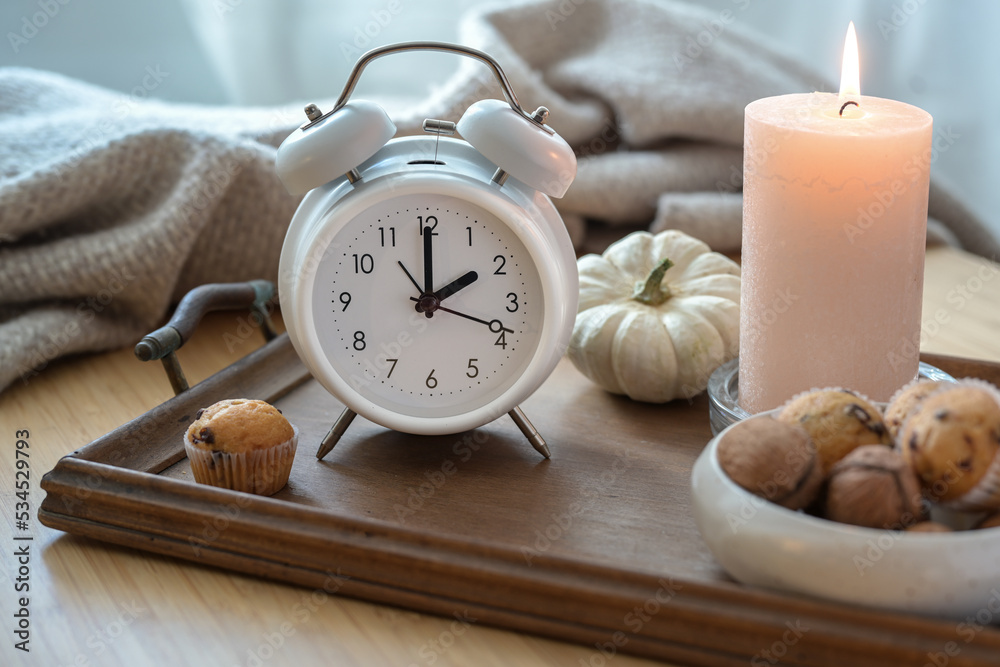 White vintage alarm clock, candle, autumn decoration and sweets on a