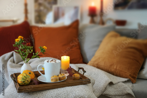 Relaxation with hot chocolate on a tray with candles and autumn decoration on the couch in a cozy living room, copy space, selected focus