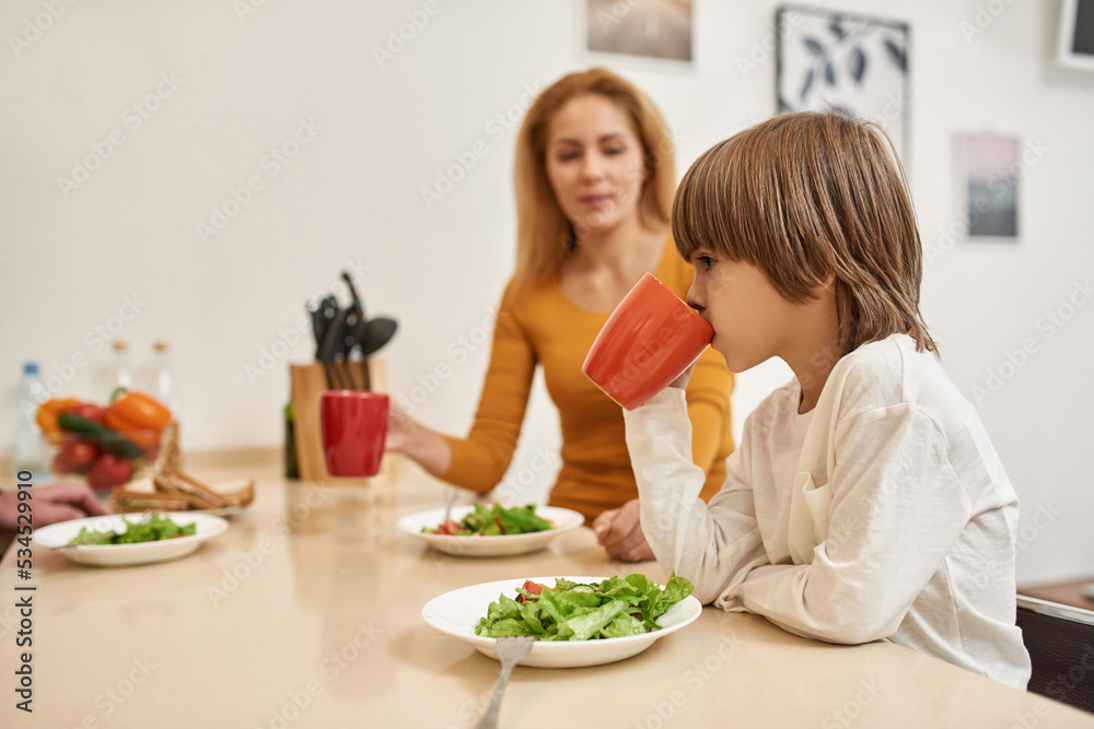 Mother looking at little boy drinking from cup