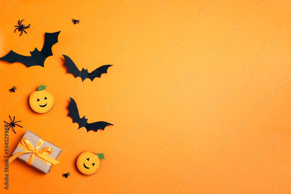 Gift box with funny pumpkins, spiders and bats on orange background.
