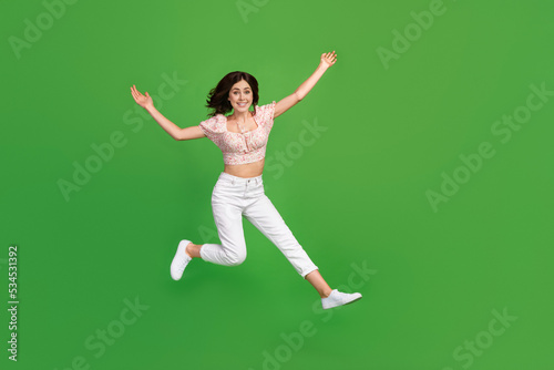 Full length photo of cute impressed girl dressed print blouse jumping high empty space isolated green color background