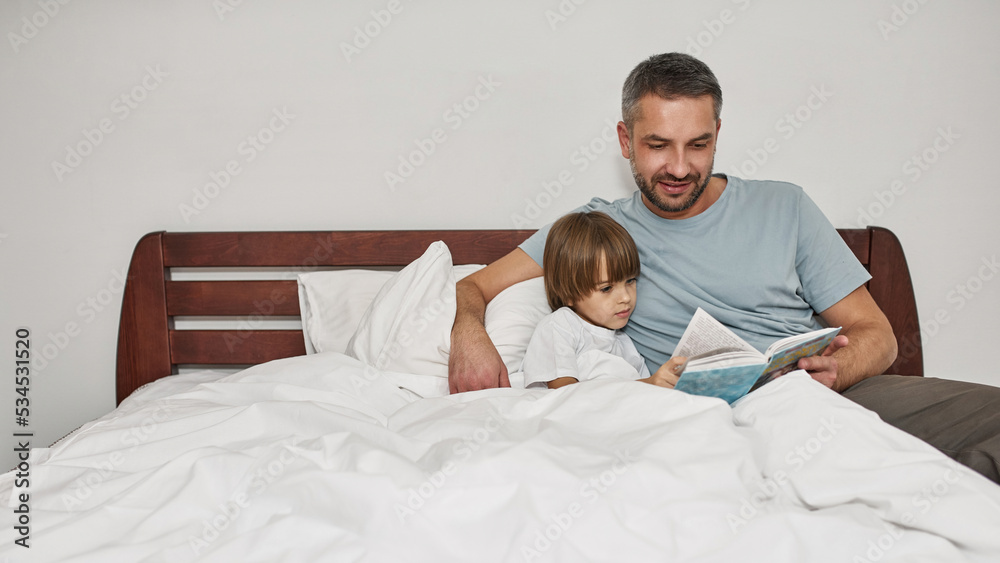 Father and little son reading book in bed at home Father and little son reading book in bed at home