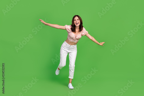 Full length photo of nice incredible girl with wavy hairdo wear white trousers top running hands wings isolated on green color background