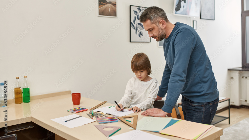 Dad look at son draw with felt-tip pen in copybook Dad look at son draw with felt-tip pen in copybook