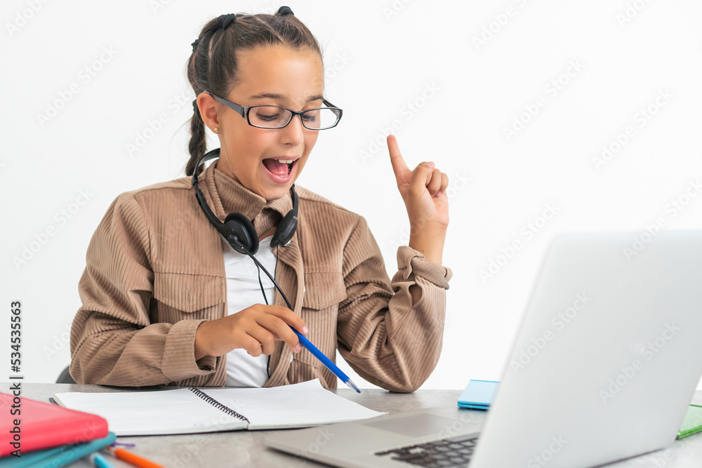 Smiling little Caucasian girl in headphones handwrite study online using laptop at home, cute happy small child in earphones take Internet web lesson or class on computer, homeschooling concept