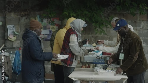 Wide shot of volunteers serving free meals for homeless at soup kitchen on street photo