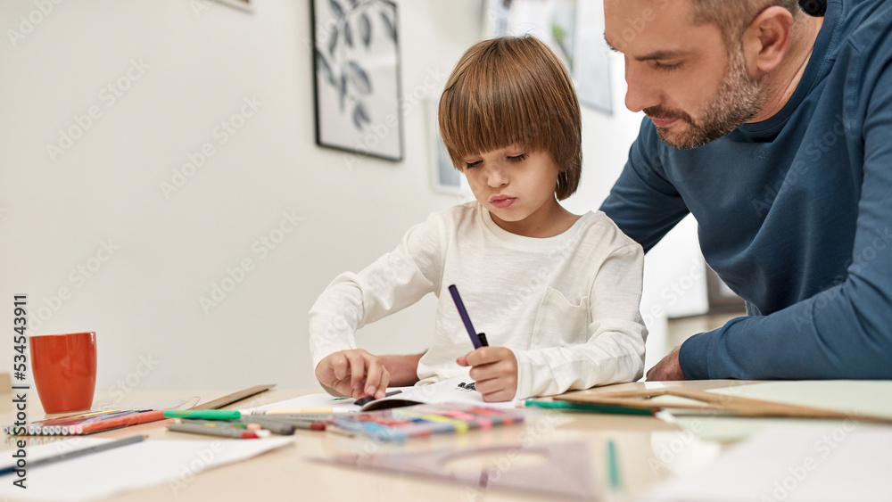 Focused father look at son draw with felt-tip pens Focused father look at son draw with felt-tip pens