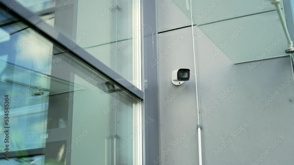 White CCTV security surveillance camera built into the metal wall of the modern glass office building outside. installed outdoor in city. Privacy, urban, protection, house system control, secure video