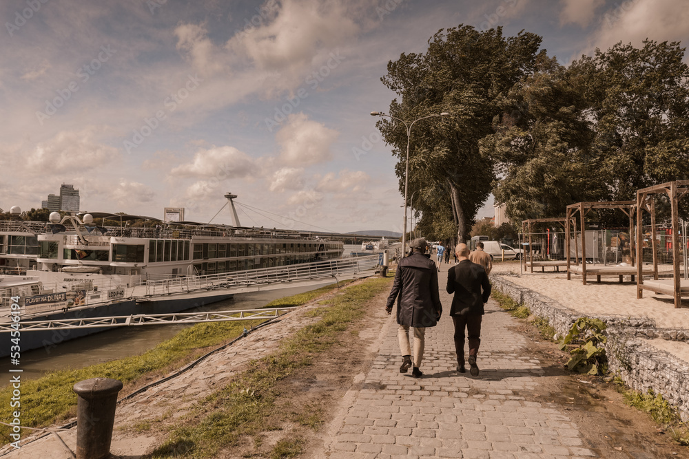 People are walking by the river in the city. Improve mental health. Rest in the city. People are walking by the river in the city. Improve mental health. Rest in the city.