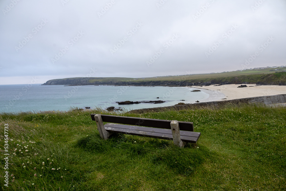 Wide angle view of Port Ness beach and a wooden bench in a looking point. Gloomy hebridean summer views.