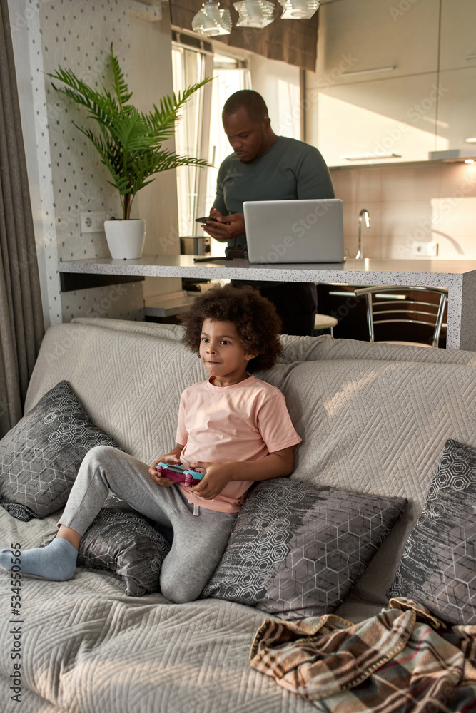 Boy playing video game and father using smartphone