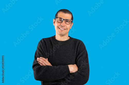 Studio shot of a man wearing casual sweater and glasses over blue background happy face smiling with crossed arms looking at the camera. Positive person.