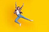 Full length photo of shiny lucky girl dressed plaid shirt jumping high rising fists isolated yellow color background