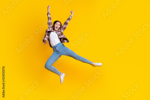 Full length photo of shiny lucky girl dressed plaid shirt jumping high rising fists isolated yellow color background