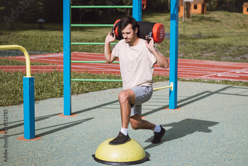 ambitious athlete is preparing for the competition season. A man with a 10kg dumbbell with water on his shoulders does a lunge on a balance beam. Training coordination and smaller muscle groups photo