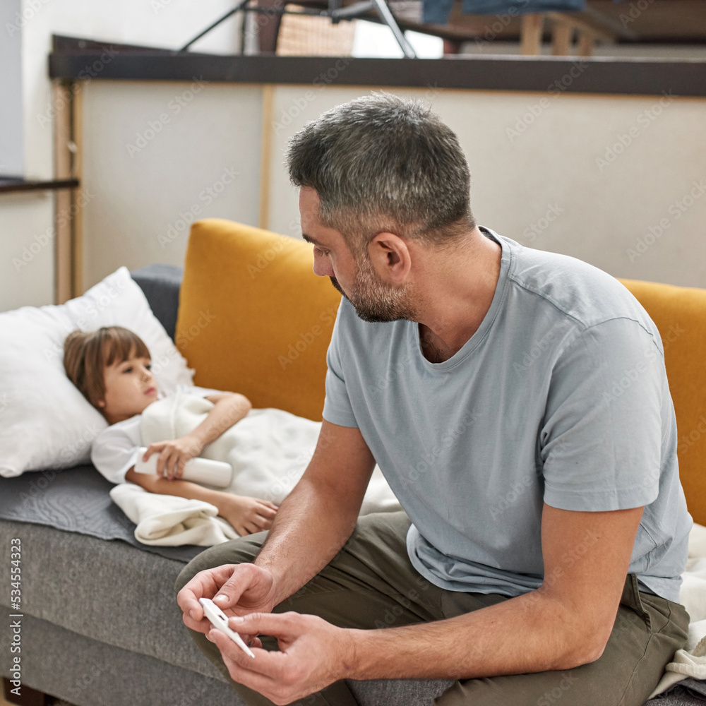 Father with thermometer look at sick son on sofa Father with thermometer look at sick son on sofa