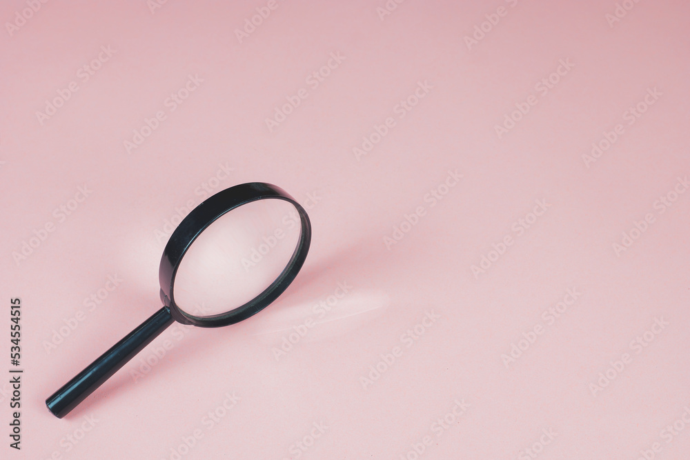 Magnifying glass on the pink background. Light is refracted through glass of magnifier. Copy space for text. Finding and zooming concept.