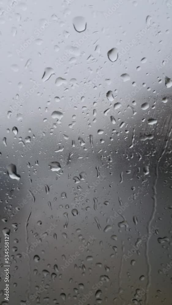 Raindrops on a glass, a window with a gray background. Rain in autumn, drops of water on the glass coming down Raindrops on a glass, a window with a gray background. Rain in autumn, drops of water on the glass coming down