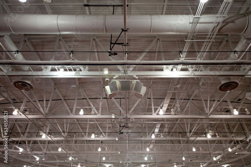 The ceiling of a large building, with air ducts and pipes, the rafters, gantry and struts, sound system speakers, lights and extractor units. photo
