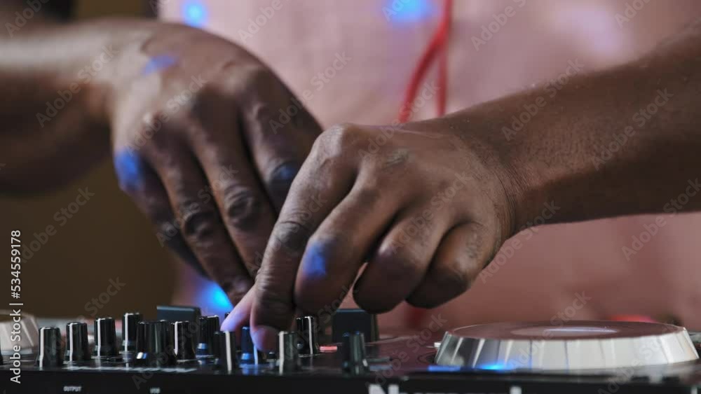 Unrecognizable unknown cool African DJ standing at mixer controller composing new sound song audio mix and rocking party in nightclub enjoying nightlife play electronic music rotates volume buttons Unrecognizable unknown cool African DJ standing at mixer controller composing new sound song audio mix and rocking party in nightclub enjoying nightlife play electronic music rotates volume buttons