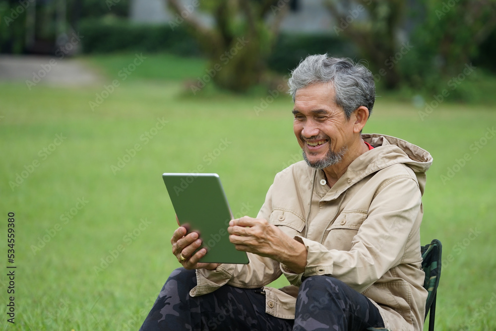 happy senior man using tablet online social media and sit on camping chair  in the garden