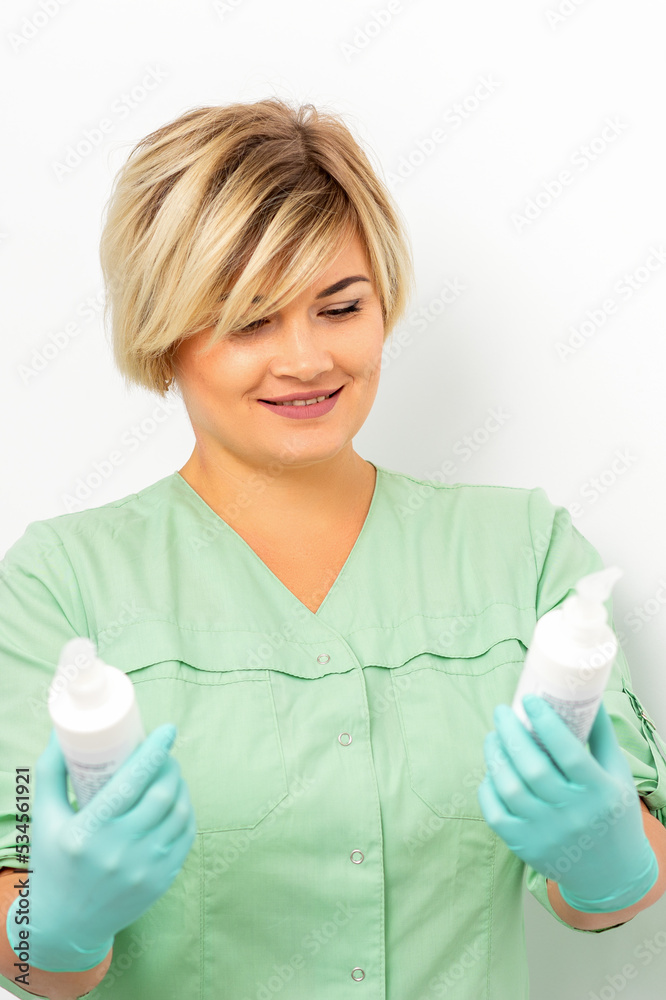 Cosmetics creams and skin care products in the hands of the female beautician smiling and standing over the white wall background Cosmetics creams and skin care products in the hands of the female beautician smiling and standing over the white wall background