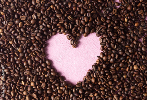 Coffee background made of beans with a pink heart laid out