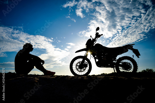 Silhouette of a lonely, heartbroken, disappointed man having a motocross bike on the mountain in a beautiful evening. Broken hearted, disappointed and lonely concept. © STOCK PHOTO 4 U