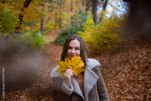 A portrait of a sweet girl with short hair enjoying the autumn weather  playing with colourful autumn leaves  having fun in autumn leaves