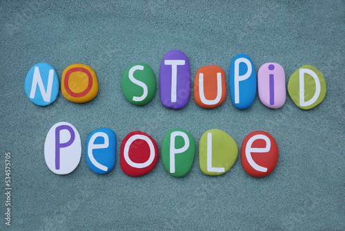 No stupid people, creative slogan composed with multi colored stone letters over green sand