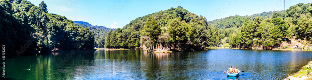 panoramic of lake with boat in the water, green forest around and blue sky in dam of the llano, villa del carbon state of mexico 