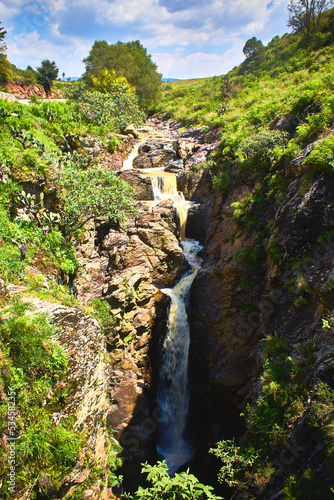 long waterfall with green vegetation and cloud sky in the mogote, el oro mexico state