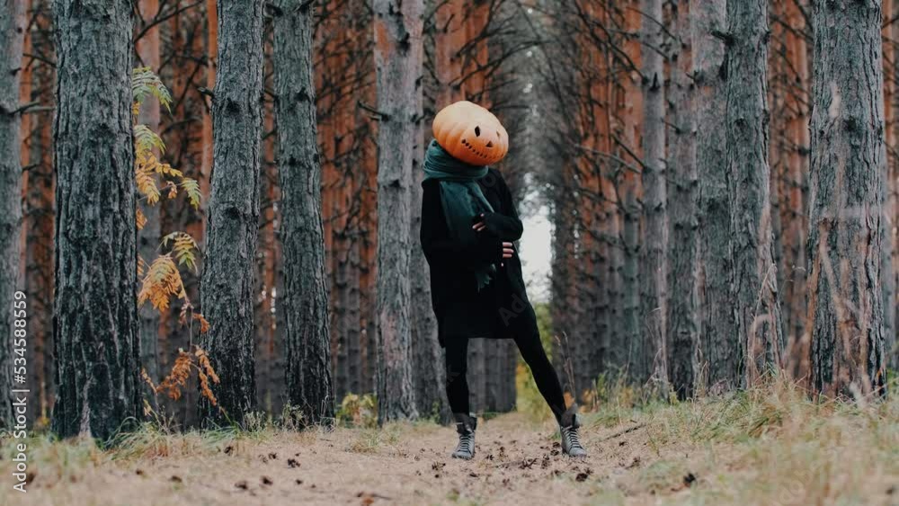 A funny girl in black clothes with a big pumpkin head dances outdoors in the forest. halloween concept A funny girl in black clothes with a big pumpkin head dances outdoors in the forest. halloween concept