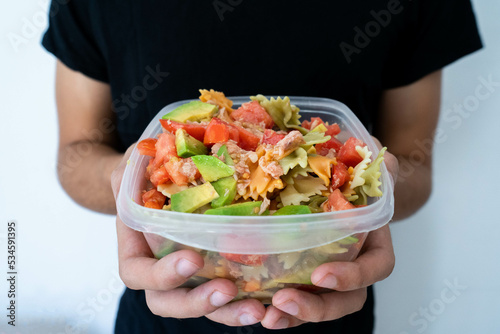 Hands holding a healthy mediterranean pasta salad tupperware