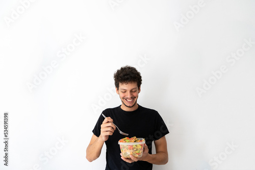 Young caucasian man eating and holding a healthy mediterranean pasta salad tupperware